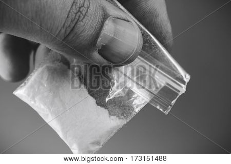 Mans hand holding or giving plastic packet with portion of cocaine or another drugs. Problems with drugs concept. Black and white photo