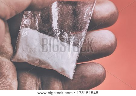Mans hand holds plastic packet with cocaine powder or another drugs. Drug dealer selling drugs junkie. Toned photo