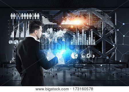 Rear view of a businessman wearing a suit and holding his smartphone while standing near a glassboard with graphs and a world map drawn on it. Toned image.