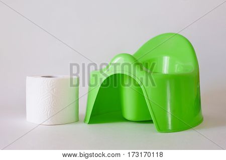 Child's green training pot and roll of toilet paper on a white background.