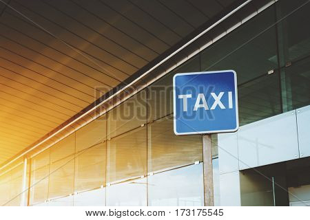 Billboard with TAXI caption with copy space area for your text message or promotional content taxi road sign near cabstand and windowed facade of airport or mall entrance on sunny day