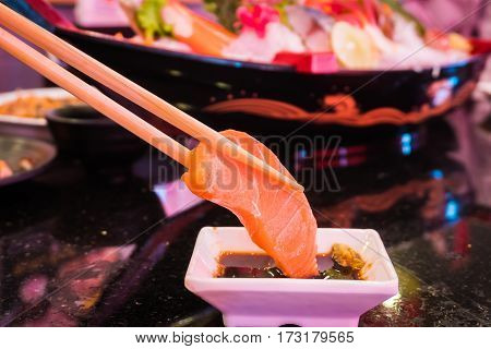 Closeup of hand with wooden chopsticks and salmon raw dip shoyu or japanese sauce and wasabi. Select focus