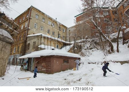 Kazan, Russia, 10 february 2017, Winter russian courtyard - old ramshackle russian house - boy cleans snow, wide angle