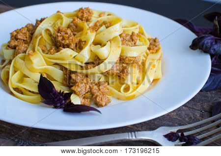Tagliatelle with bolognese sauce on wooden background. Traditional Italian pasta Bolognaise with a spicy tomato based meat sauce garnished with fresh basil. Selective focus.