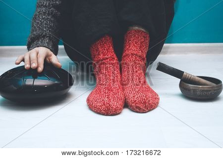 Man in a red woolen socks sitting on the floor in the yoga studio with a singing bowl and steel tongue drum