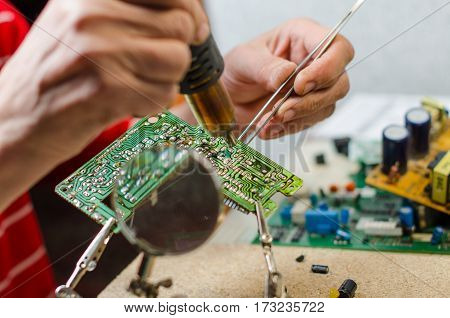 Engineer soldering microcircuit though magnifier. third hand tools