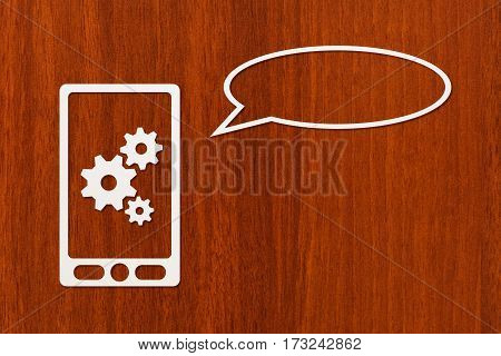 Paper tablet or smartphone with cogwheels and speech bubble copyspace dark wooden background. Abstract conceptual image
