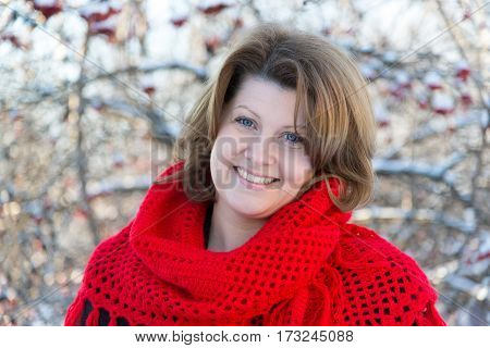 A woman in a red shawl in the winter is on the background of viburnum