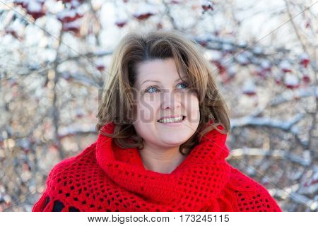 A woman in a red shawl in the winter is on the background of viburnum