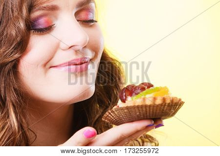 Bakery sweet food indulging and people concept. Cute attractive woman closed eyes holds cake cupcake in hand smelling yellow background