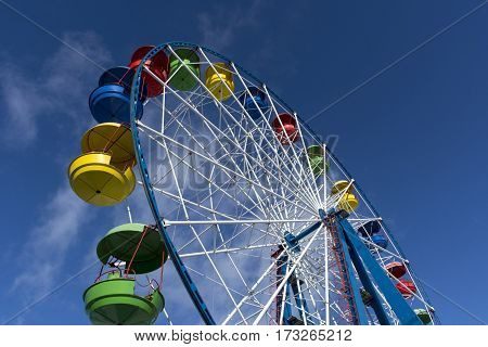 Ferris wheel with colored cabins on the blue sky background Sunny day clouds ride fair fun