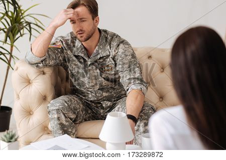 Something is better to forget. Handsome sad bearded soldier holding his forehead and having bad memories while trying to cope with a posttraumatic stress
