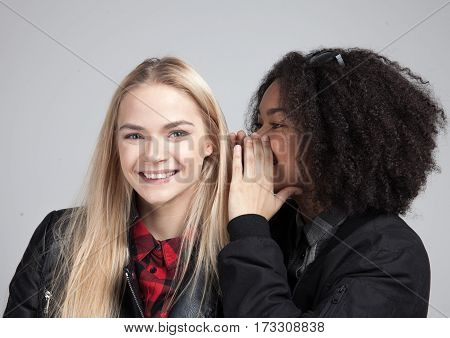 Two teenage hipster girls in studio. One says the other some horrifying secret. Isolated on white background.