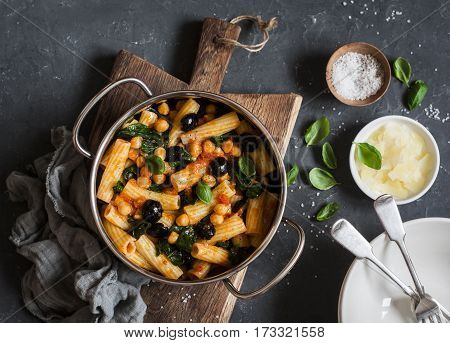 Rigatoni pasta with chickpeas spinach and olives in a tomato sauce on a dark background top view. Vegetarian food concept
