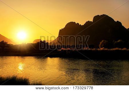 Sunset over Nam Song River with silhouetted rock formations in Vang Vieng Laos. Vang Vieng is a popular destination for adventure tourism in a limestone karst landscape.