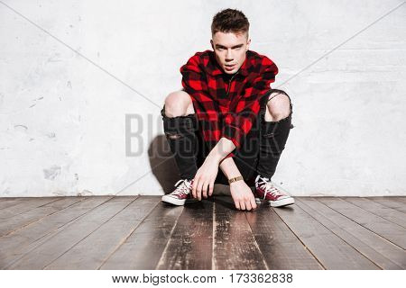 Hipster in shirt sitting near the wall and looking at camera