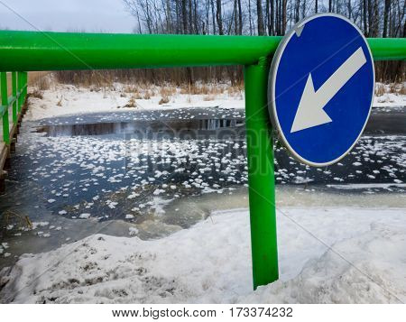 River under bridge with thin ice and blue arrow sign