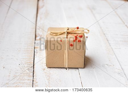 Gift box wrapped in craft paper tied with twine tender small red flower white plank wood background minimalistic copyspace kinfolk