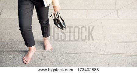 Young woman rubbing her sore tired feet. Businesswoman in office style clothes carrying in hand her high heel shoes walking barefoot step up legs close-up copy space or background for banner