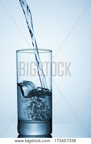 Sparkling water pouring into glass on blue background