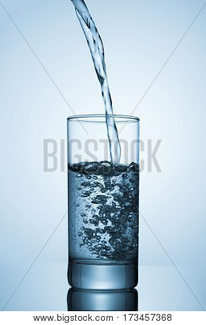 Sparkling water pouring into glass on blue background