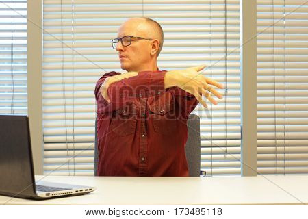 middle age balding man relaxing neck - stretching arm - short break for exercise on chair in office
