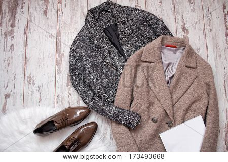 Two woolen coat brown patent leather shoes on a white fur white blank sheet a wooden background. Fashion concept. top view