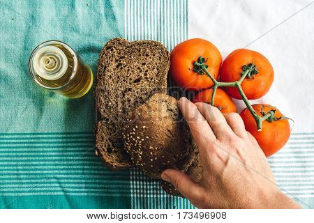 Hand over on Olive oil tomato and slides of brown bread on tablecloth. Top view