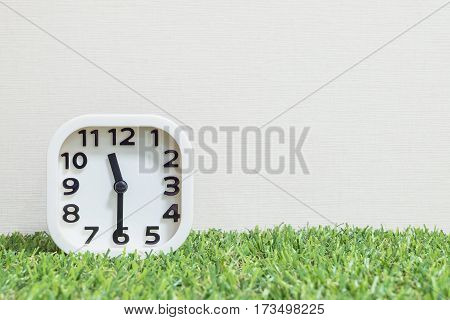 Closeup white clock for decorate show a half past eleven or 11:30 a.m. on green artificial grass floor and cream wallpaper textured background with copy space