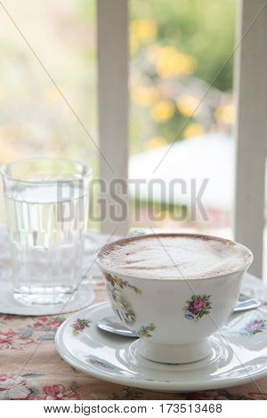 Cafe art latte coffee in the vintage cup on the tabel with a glass of water on the table