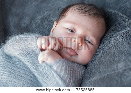 Newborn baby wrapped in knitted warm blanket. Beautiful closeup portrait of a newborn baby who is awake and looks around. The kid pulled the handle of the blankets.