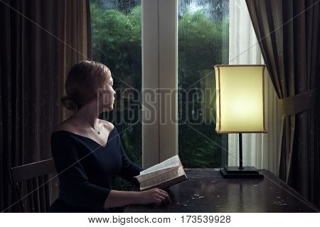 portrait of young woman with book sitting by the window