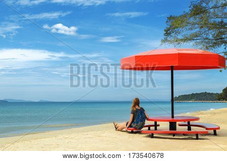 Young woman is resting under a beach umbrella and is looking at the sea, Sihanoukville, Cambodia