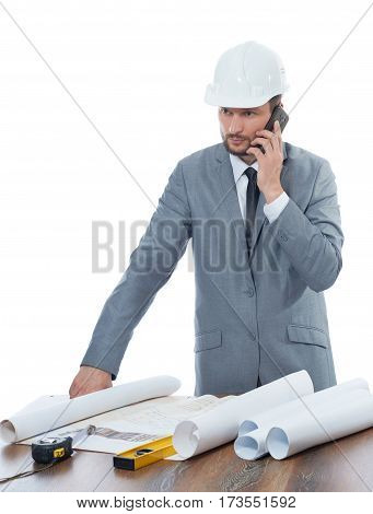 Important calls. Professional male engineer talking on his mobile phone while working on building blueprints isolated on white profession development technology connectivity mobility business concept