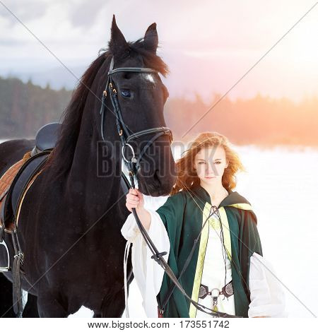 Young girl in white dress with black thoroughbred horse on winter field. Historical equine background