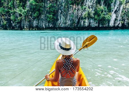Woman paddling a kayak in the island lagoon between mountains. Kayaking in El Nido, Palawan, Philippines.