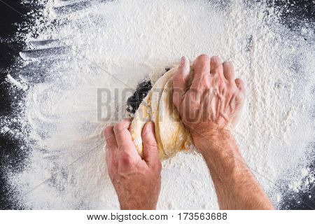 Baking concept. Flour, milk, butter, yeast and eggs carton on rustic wooden table, cooking ingredients. Unrecognizable man's hands top view knead dough on black background. Male baker