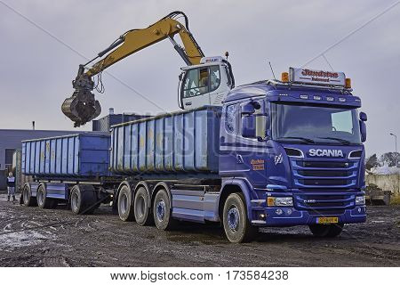 SNEEK, THE NETHERLANDS - MARCH 6, 2017: A mobile crane with hydraulic elevated cab and equipped with a sorting grapple is loading a container on lorry trailer with debris. Focus on first container.