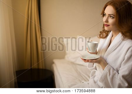 Red-haired girl with a cup of coffee in bed
