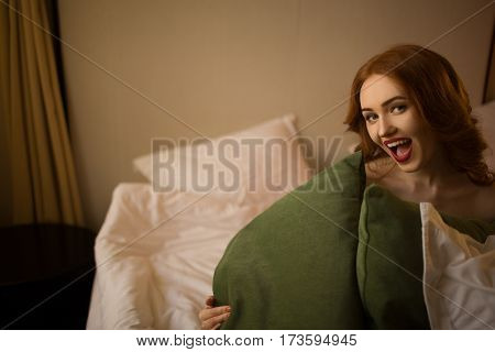Joyful red-haired girl in bed with pillows