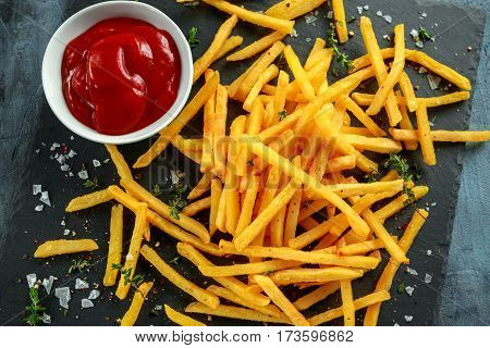 French fries with sea salt, cracked pepper and ketchup on stine board.