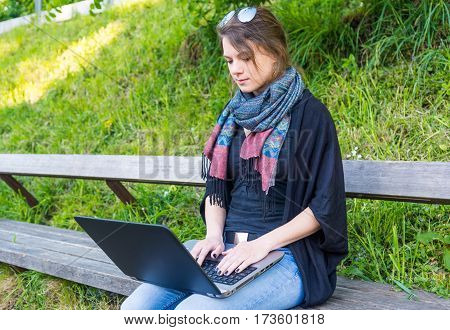 Young woman using laptop at a riverbank. Milleanial working in a park.