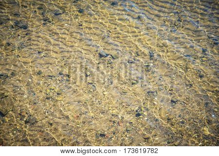water background with yellow sand and pebbles on the bottom in sunlight