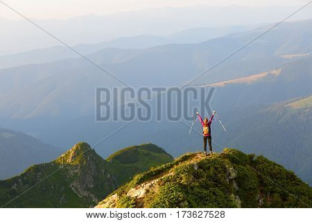 Sporty girl with back sack is standing at the edge of the precipice and watching on the endless vast of mountains landscape in the sunny day.