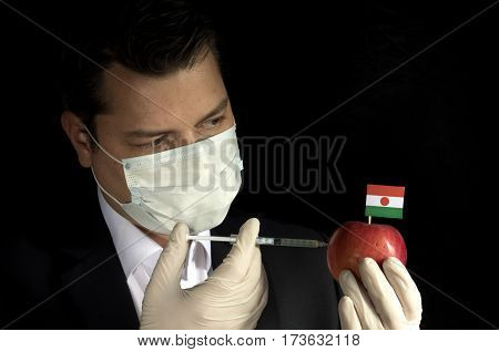 Young Businessman Injecting Chemicals Into An Apple With Nigerien Flag On Black Background