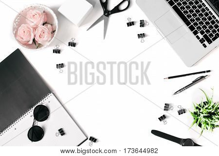 White office desk frame with laptop keyboard and supplies. Laptop, notebook, pen, roses, plant, sunglasses, clips, pencil, scissors, watch and office supplies on white background. Flat lay, top view, mockup