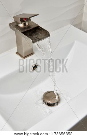 Running water from brushed nickel faucet on top of the white modern vanity and marble sink.