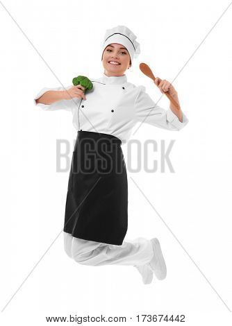Young woman chef with broccoli and wooden spoon in hands jumping on white background