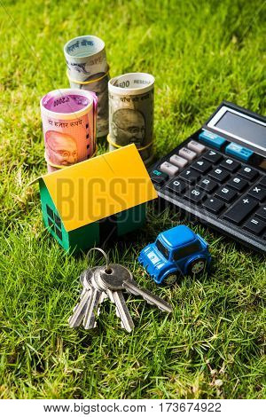 indian currency notes of rupees 100, 500 and 2000 in roll or stack with small home model, keys, toy car and calculator with blank board over green grass - home buying and finance concept in India