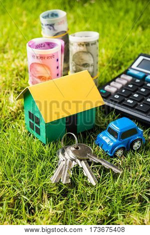 indian currency notes of rupees 100, 500 and 2000 in roll or stack with small home model, keys, toy car and calculator with blank board over green grass - home buying and finance concept in India